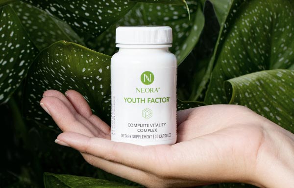 A woman holding up a Youth Factor® Complete Vitality Complex bottle in front of a giant leaf.
